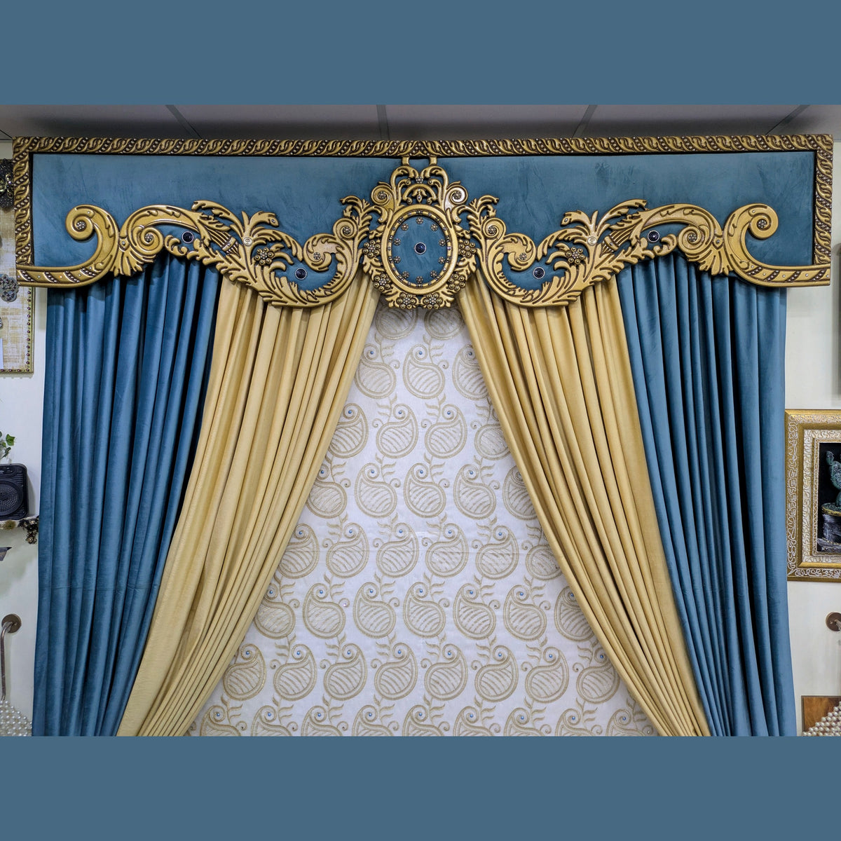 An ornate theatrical curtain set featuring blue velvet side drapes, a central cream patterned drape, and a decorative gold and blue valance with elaborate scrollwork.